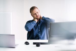 Young Businessman In Office At Desk Suffering From Neck Pain